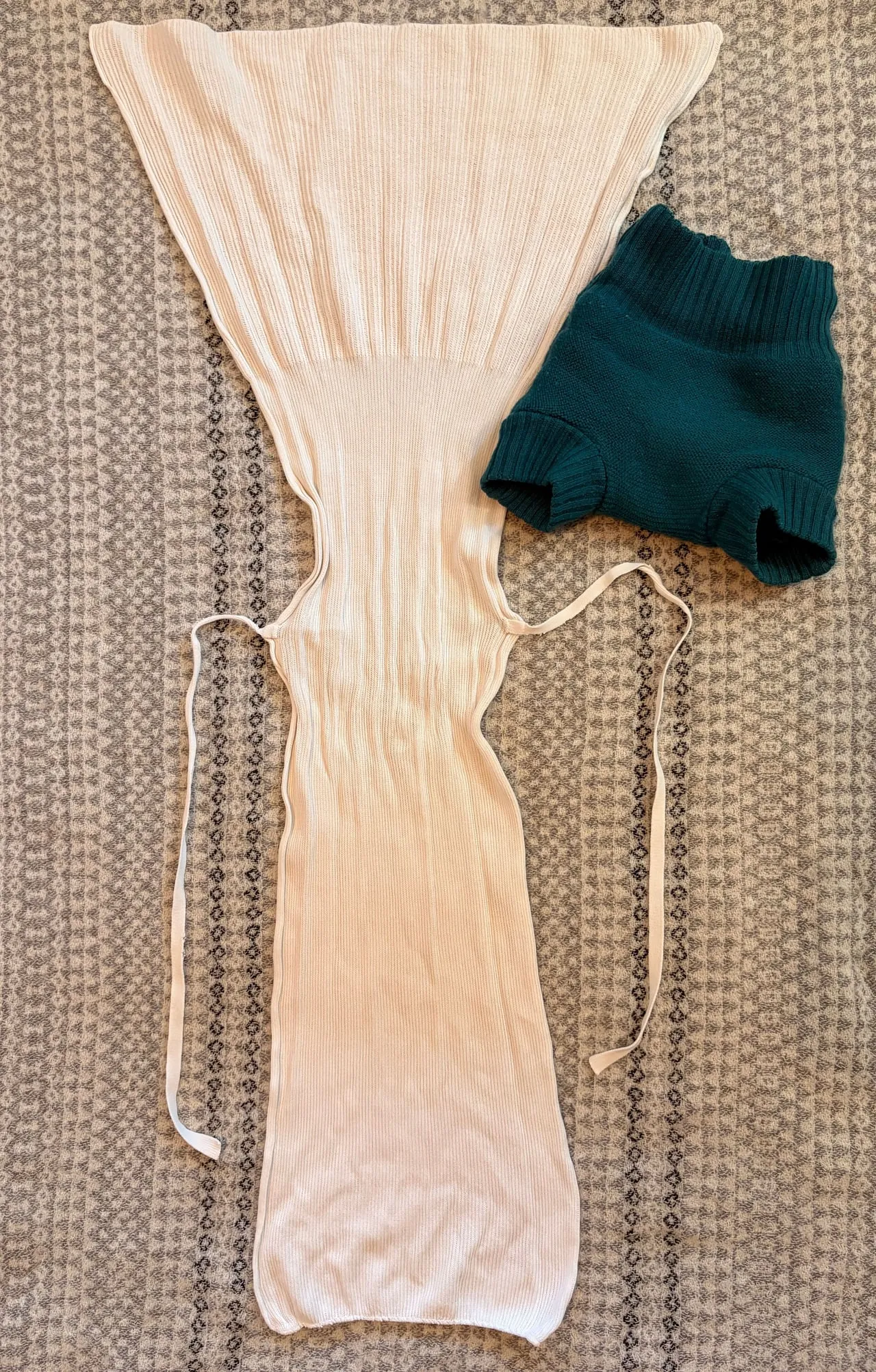 An unfolded cream Disana cotton tie nappy, with its long ties laid out and a teal wool cover beside it