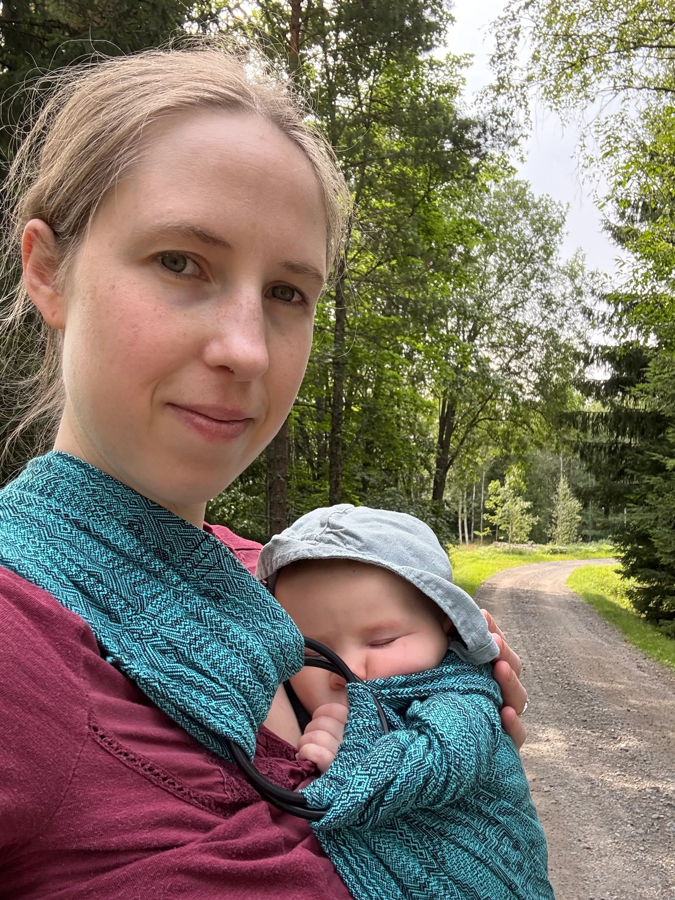 Sara carrying her sleeping baby in a ring sling on a woodland road