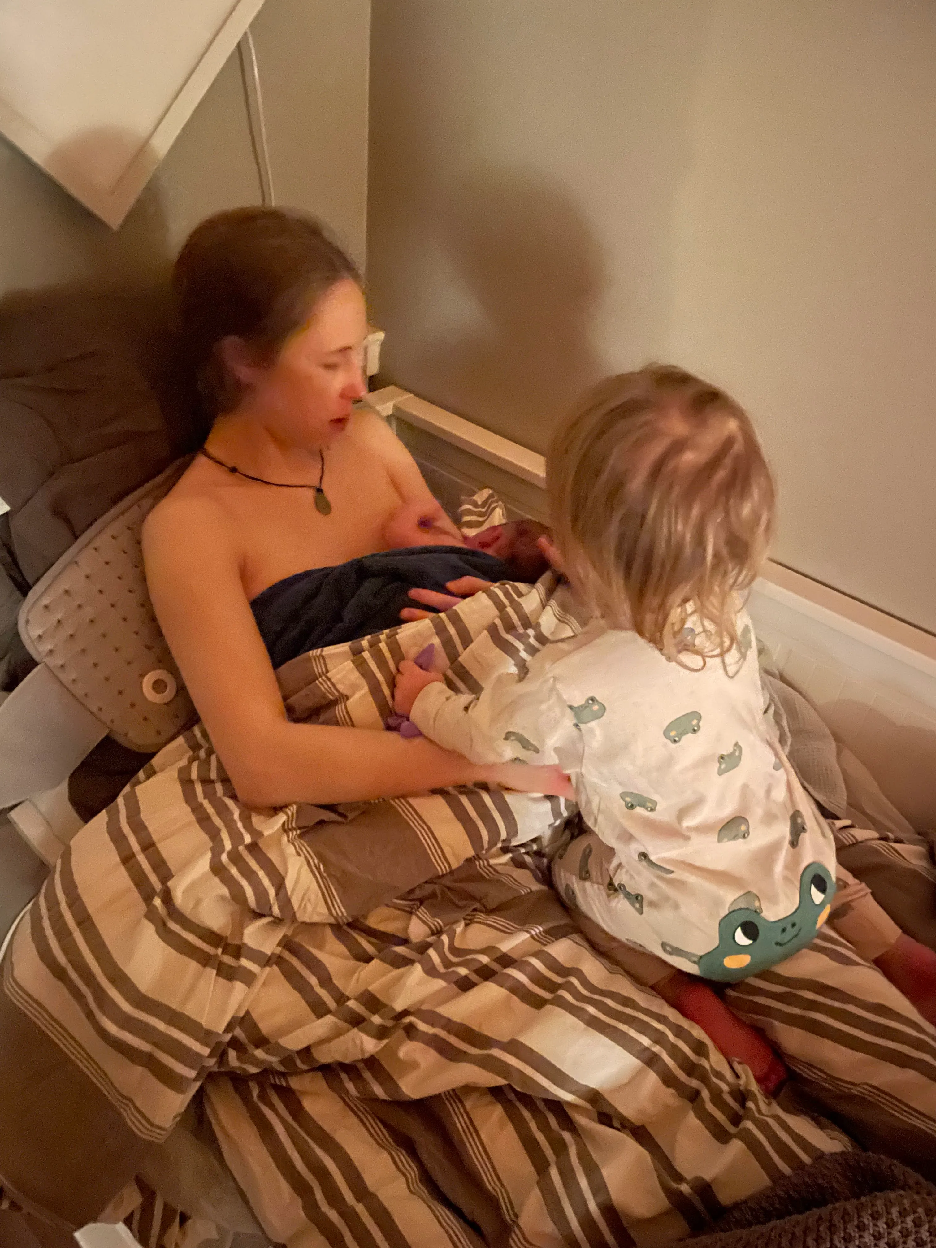 Sara resting in bed with her newborn son while her daughter sits beside them
